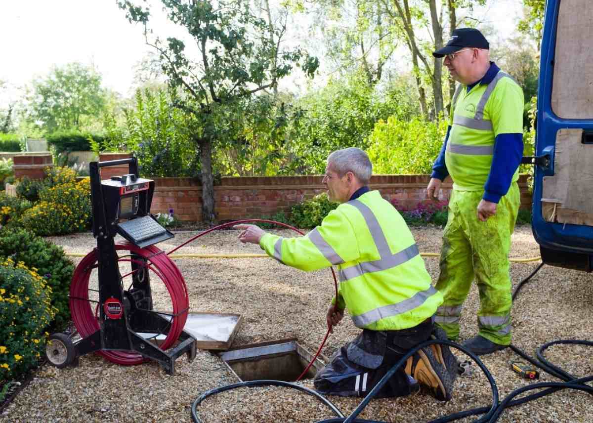 A sewer camera inspection is being conducted by two professionals.